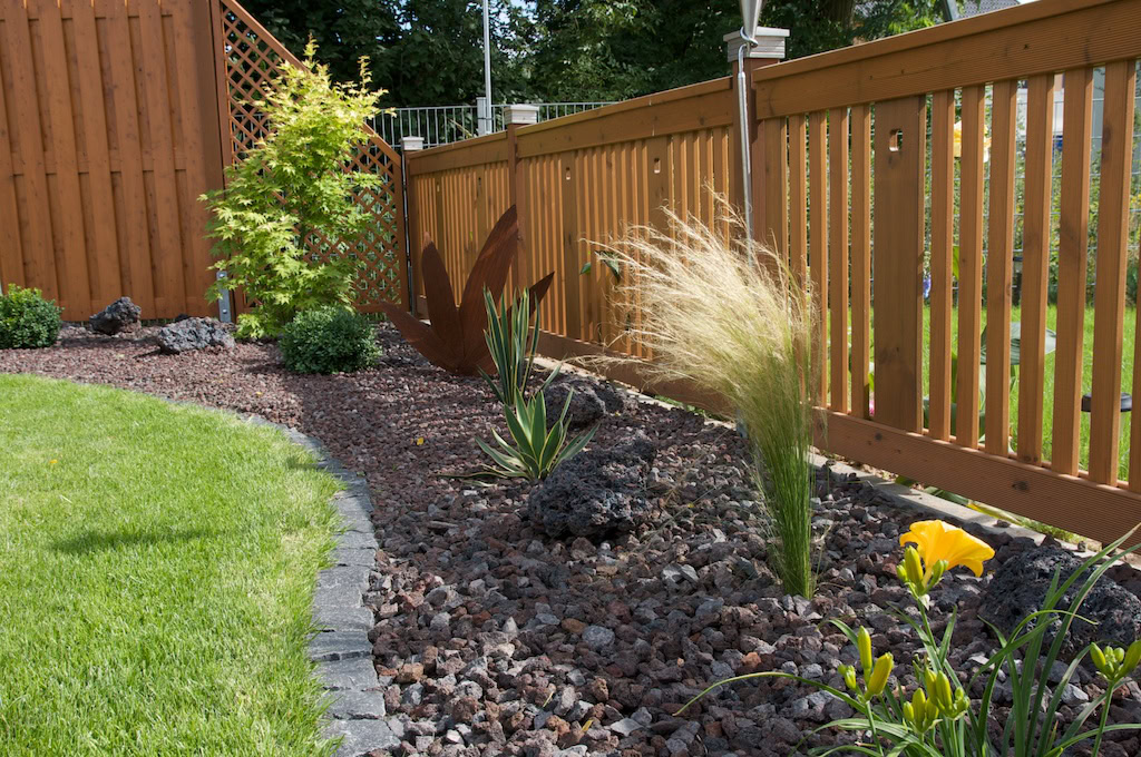 Garten mit Holzzaun und Pflanzen im Kiesbeet